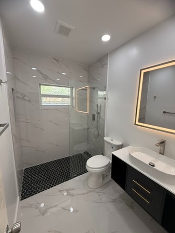 Completed luxury bathroom remodel with marble porcelain tile walls and LED backlit mirror in Glenvar Heights