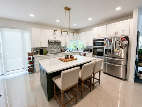 Beautiful two-tone kitchen renovation in Lakes of the Meadow, featuring custom white and green cabinets, geometric tile backsplash, and a branch gold chandelier